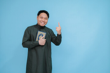 Asian Muslim man expressing himself hugging and kissing the holy book of the Koran during the month of Ramadan wearing green Arabic robe
