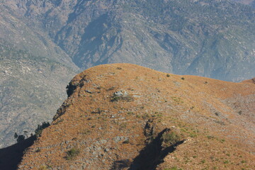 Golden dry grassy mountain peak under bright sunlight with rugged rocky slopes in the background