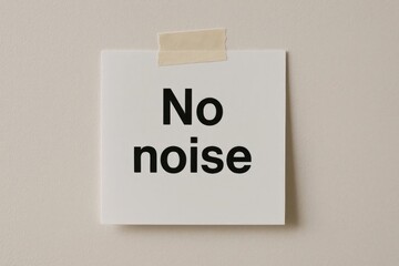 A white note with the text 'No noise' written in bold black letters. The note is taped to a beige wall, conveying a message about quietness.