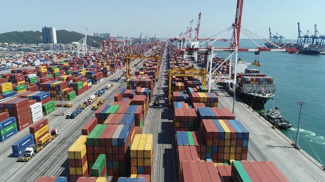 Container terminal aerial view with stacked cargo container rows quay cranes loading ship industrial port activity turquoise sea clear sky container yard with stacked shipping container rows cargo