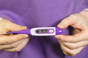 Woman holding electronic thermometer with high body temperature 39.3 degrees.