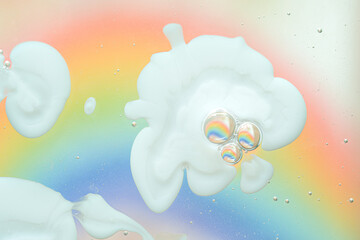 Soft macro shot of white liquid shapes and clear bubbles on bright rainbow gradient background,...