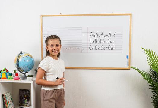 Cheerful girl studies alphabet and handwriting using a magnetic wall board. Concept of homeschooling, literacy skills, focused learning, positive emotions and child development.