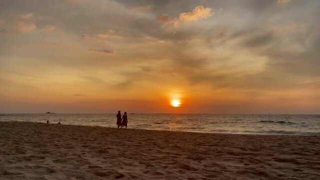 Silhouetted couple walking along a sandy beach at sunset with calm ocean and warm sky tones, tropical travel and romance, travel, vacation, relaxation, summer lifestyle, and peaceful moment concepts