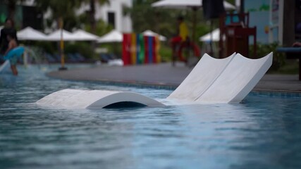 Two white sun loungers submerged in water in a hotel swimming pool