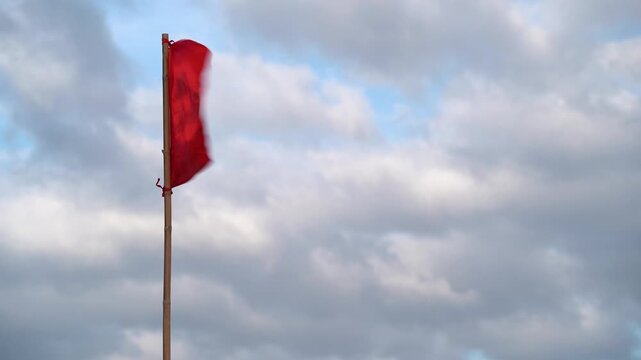 A red beach flag flutters in the wind against a blue sky with clouds