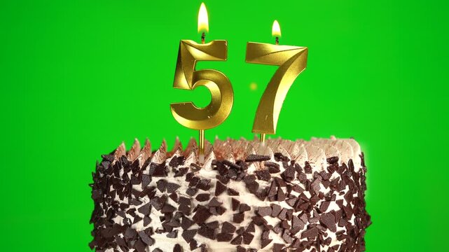 Lighting number 57 golden birthday candle on festive cake. Green screen, chromakey. Birthday cake on 57th anniversary