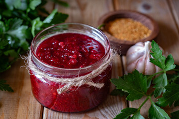 Cranberry sauce in a small jar on a wooden table. Spicy sauce for meat dishes. Close-up