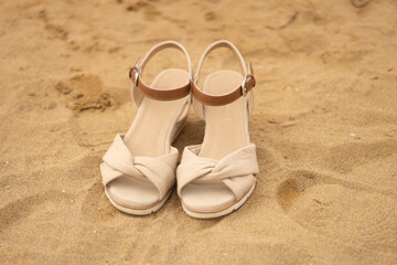 weiße Damenschuhe, Sandalen, stehen an einem Sandstrand