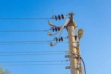 Concrete utility pole with electrical wires, insulators and street lamp against clear blue sky. Low...
