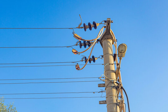 Concrete utility pole with electrical wires, insulators and street lamp against clear blue sky. Low angle view of power lines and infrastructure.