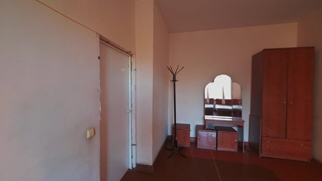 Spacious room with wooden wardrobe, coat rack, vanity table with mirror, small cabinets, light-colored walls, tiled floor, minimal furnishing, neutral tones