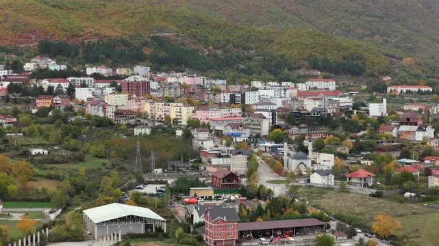 Aerial video of Bajram Curri, showing homes, farmland and the town center set against the steep forested slopes and rugged peaks of the Albanian Alps. 
