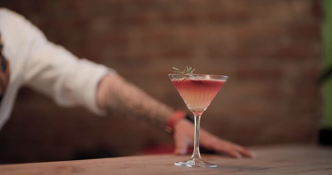 Barman prepares cocktail at bar countertop during evening shift in vibrant location with close-up of glass and hand reaching for drink