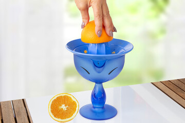 Womens hand making fresh orange juice with lemon squeezer which stands on table. Abstract spring background. Multifunctional juicer, lemon squeezer, lemon juicer, rotary press for limes.
