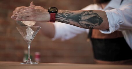 Expert bartender carefully adds ice to a martini glass, highlighting mixology and cocktail artistry in slow motion.