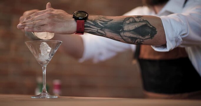 Expert bartender carefully adds ice to a martini glass, highlighting mixology and cocktail artistry in slow motion.