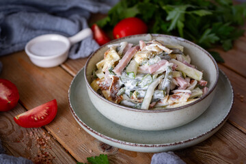 A hearty salad with ham, egg, and vegetables on a beautiful plate on a wooden table. Salad with mayonnaise for dinner. Close-up