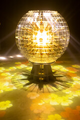 Obraz premium A glowing spherical transparent globe shaped lamp stands on a metal base radiates warm golden light in a dark room