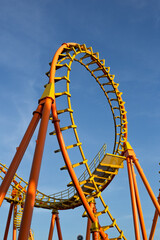 A thrilling amusement park ride features a bold circular loop roller coaster rises against a clear blue sky background. .