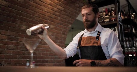 Bartender Pours a Mixed Drink into a Martini Glass at a Brick-Walled Bar