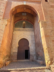 Fototapeta premium The monumental Gate of Justice towers overhead with its grand horseshoe arch and a niche statue of the Virgin Mary, marking the main entrance to the historic Alhambra fortress in Granada, Spain.