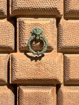 A heavy bronze lion-shaped door knocker hangs on a wall of large rusticated stone blocks, highlighting the Renaissance architecture of the Palace of Charles V in the Alhambra, Granada, Spain.