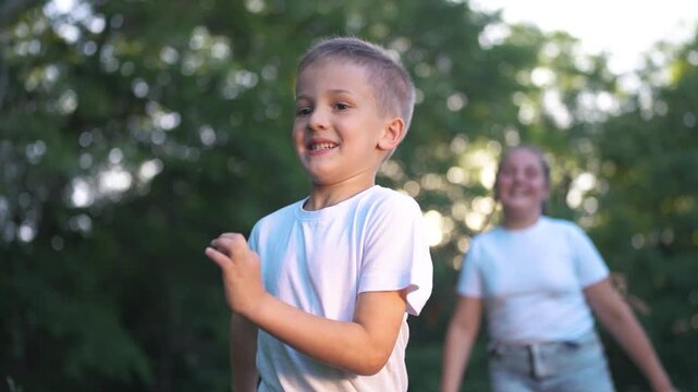 Young boy running in the grass. A boy running outdoors with a tree. A young girl is playing with the sunlight and is energetic and playful in summer. A young boy dashing through the grass lifestyle.