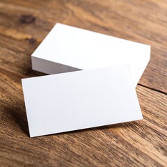 Two pristine white business cards are elegantly placed on a rustic wooden table, showcasing their smooth texture and minimalist design against the warm wood grain.