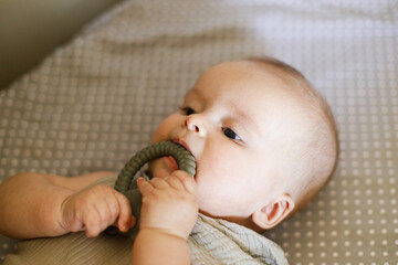 Cute baby lying in crib with  little teether, close up. Teething. Sweet infant portrait in bassinet with silicone toy. Childhood, Love and care concept.  Time for sleep.