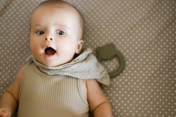 Cute happy baby lying in crib with teether, top view with coy space. Teething. Sweet infant portrait in bassinet with silicone toy. Childhood, Love and care concept.