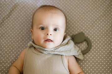 Cute happy baby lying in crib with teether, top view with coy space. Teething. Sweet infant portrait in bassinet with silicone toy. Childhood, Love and care concept.