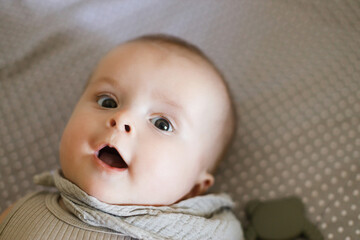 Cute happy baby lying in crib, close up. Sweet infant smiling portrait in grey bassinet, space for text. Childhood, Love and care concept. Time for sleep.