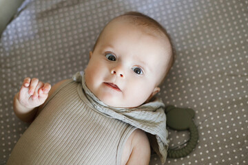 Cute happy baby lying in crib with teether, top view with coy space. Teething. Sweet infant portrait in grey bassinet with silicone toy. Childhood, Love and care concept.