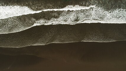 Abstract aerial lines of ocean waves on dark sand beach in Costa Rica at overcast dusk.