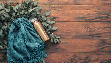 Eucalyptus leaves and cozy teal blanket with a metal water bottle on a rustic wooden background