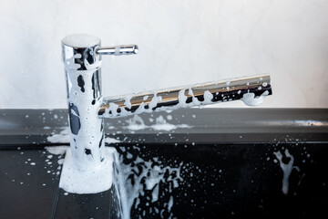 Water dripping and foam for cleaning on metal tap. Durty faucet in kitchen.