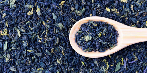 Dried butterfly pea flowers and tea leaves on a wooden spoon, creating a beautiful vibrant blue background texture