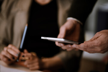 Meeting in a modern office with a man handing a smartphone to a colleague while a woman observes, showcasing collaboration and technology in a dynamic work environment