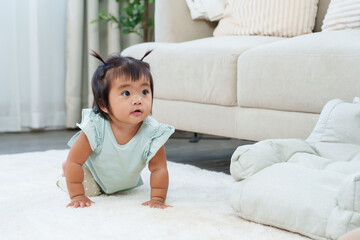 Fototapeta premium Sweet asian toddler girl crawling on white carpet looking forward with curious face during home playtime showing early development movement exploration and happiness of growing childhood lifestyle