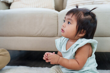 Fototapeta premium Cute asian toddler girl sitting on floor looking upward with curiosity during home playtime showing focus awareness and early learning development expressing innocence growth and exploration moment