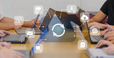 オフィスでノートパソコンを並べて作業する会議風景、クラウド同期と情報共有を表すビジネスシーン、DX