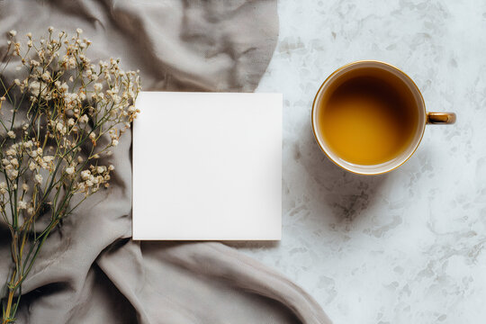 cup of tea beside a blank card and dried flowers on a gray cloth