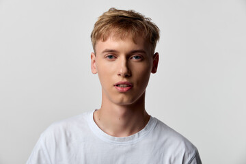 Fototapeta premium Young man wearing a white tee against a neutral backdrop, close up facial expression, casual studio shot for fashion, clean minimal background suitable for lifestyle branding