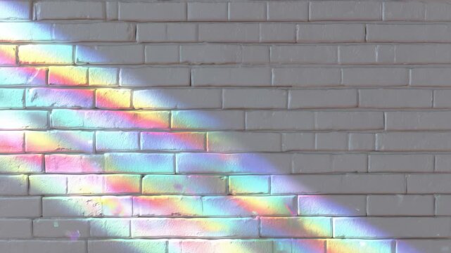 Colorful light shines on a brick wall with a rainbow pattern created by sunlight during the day in an indoor space with plain decor