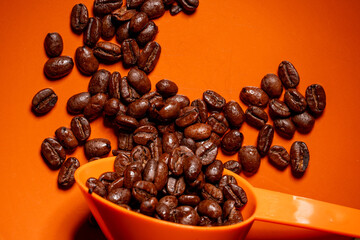 Whole coffee beans orange background and scoop