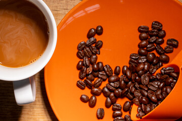 Top down shot of a cup of coffee with whole beans on orange background food concept