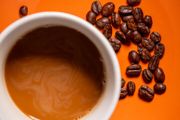Top down shot of a cup of coffee with whole beans on orange background food concept