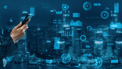 A businessman holds a smartphone while digital graphs and charts emerge around him, set against a beautiful urban skyline at night, symbolizing advanced technology and data analysis. Xenic