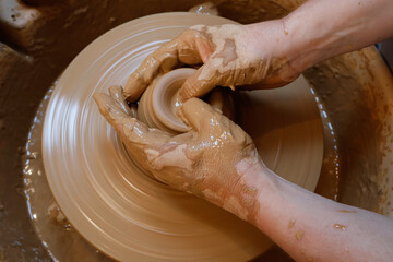 Fototapeta premium Woman´s hands shaping clay on pottery wheel in ceramic workshop. Small business concept